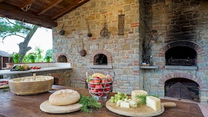 An outdoor kitchen area with stone walls, a brick oven, and a variety of food items displayed on wooden boards.