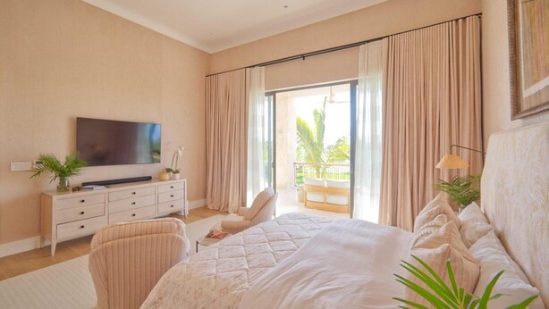 A bedroom with a bed, a TV, a desk, a chair, and a balcony with curtains. - Luxury Villa With Heated Pool Jacuzzi Full Staff (Punta Cana)