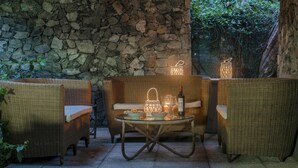 A stone wall, wicker furniture, a table with a bottle and glasses, and lanterns. - Villa Liberty Albisola 6 2 Emma Villas (Albisola Superiore)