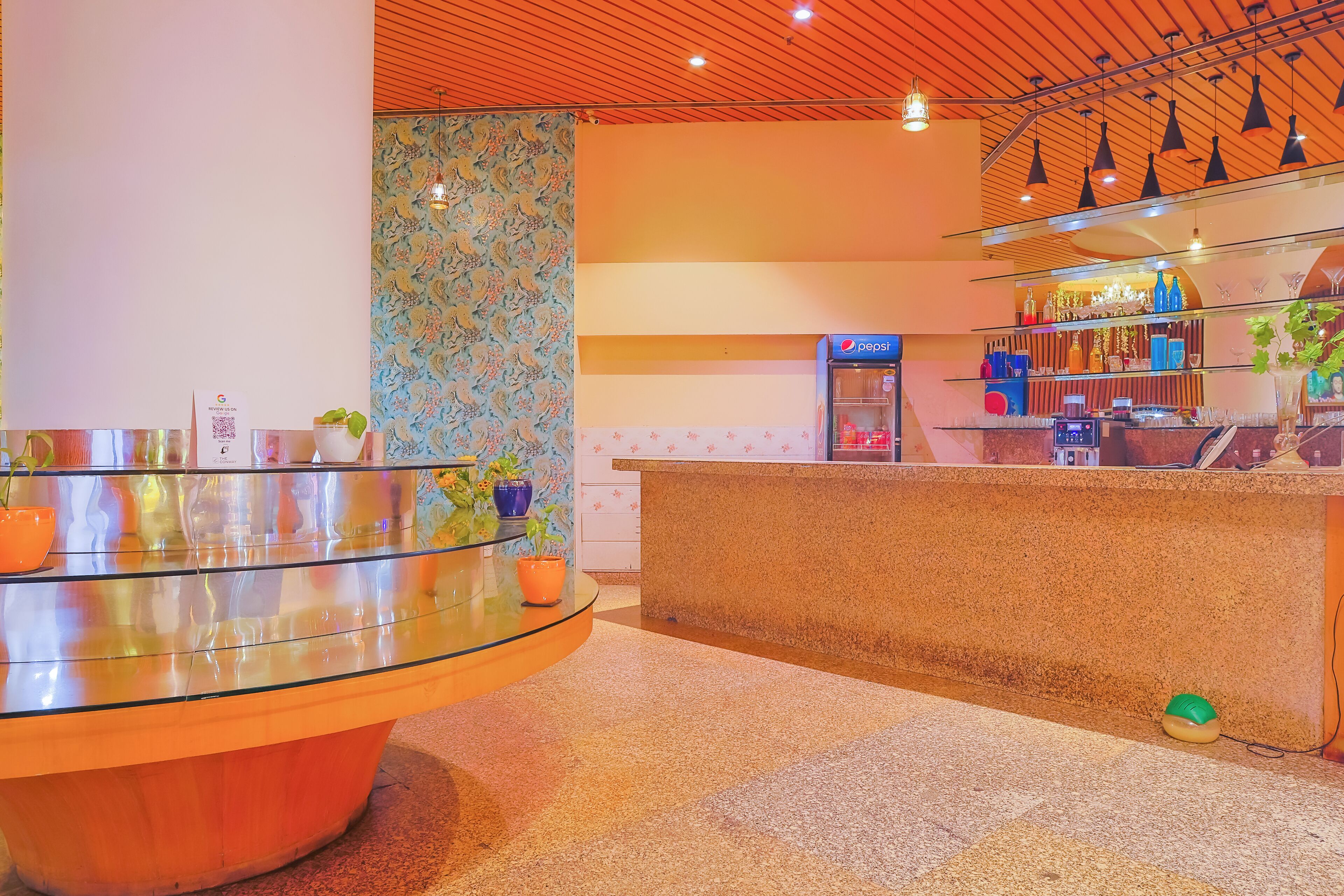 Een moderne hotel lobby met een gebogen receptiebalie, een Pepsi-koelkast en diverse decoratieve objecten op planken.