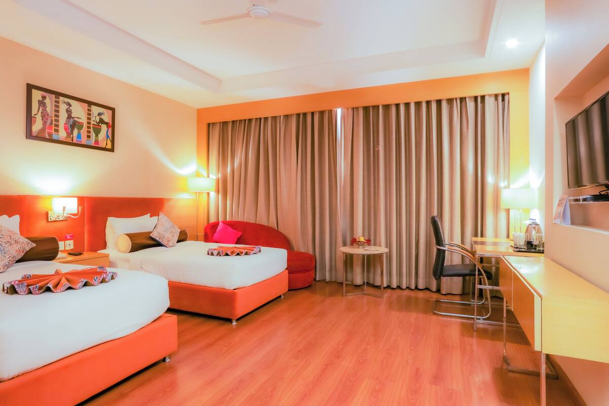 A hotel room with two beds, a desk, a chair, a small table, and a large window with curtains.