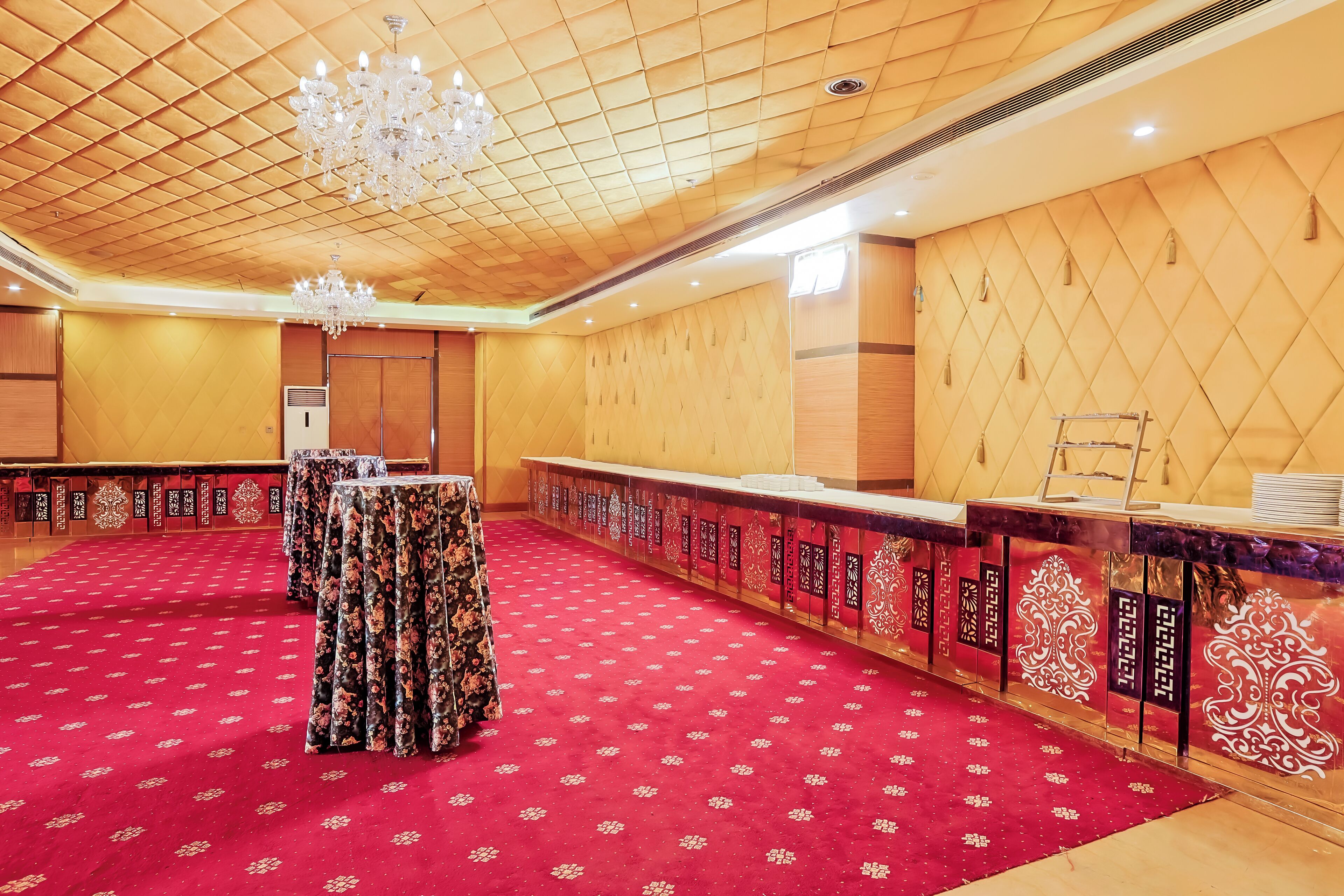Una sala de conferencias con alfombra roja, paneles de madera, una araña y una larga mesa con mantel de flores.