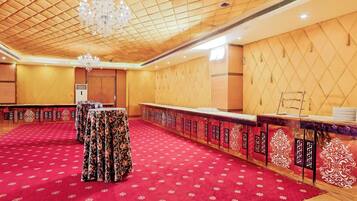 Una sala de conferencias con alfombra roja, paneles de madera, una araña y una larga mesa con mantel de flores.