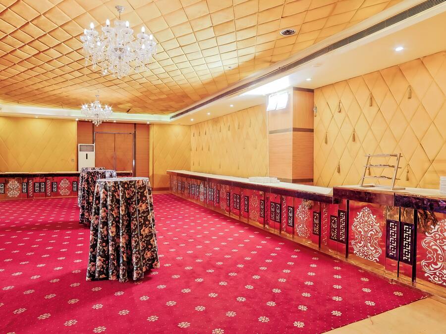 Una sala de conferencias con alfombra roja, paneles de madera, una araña y una larga mesa con mantel de flores.