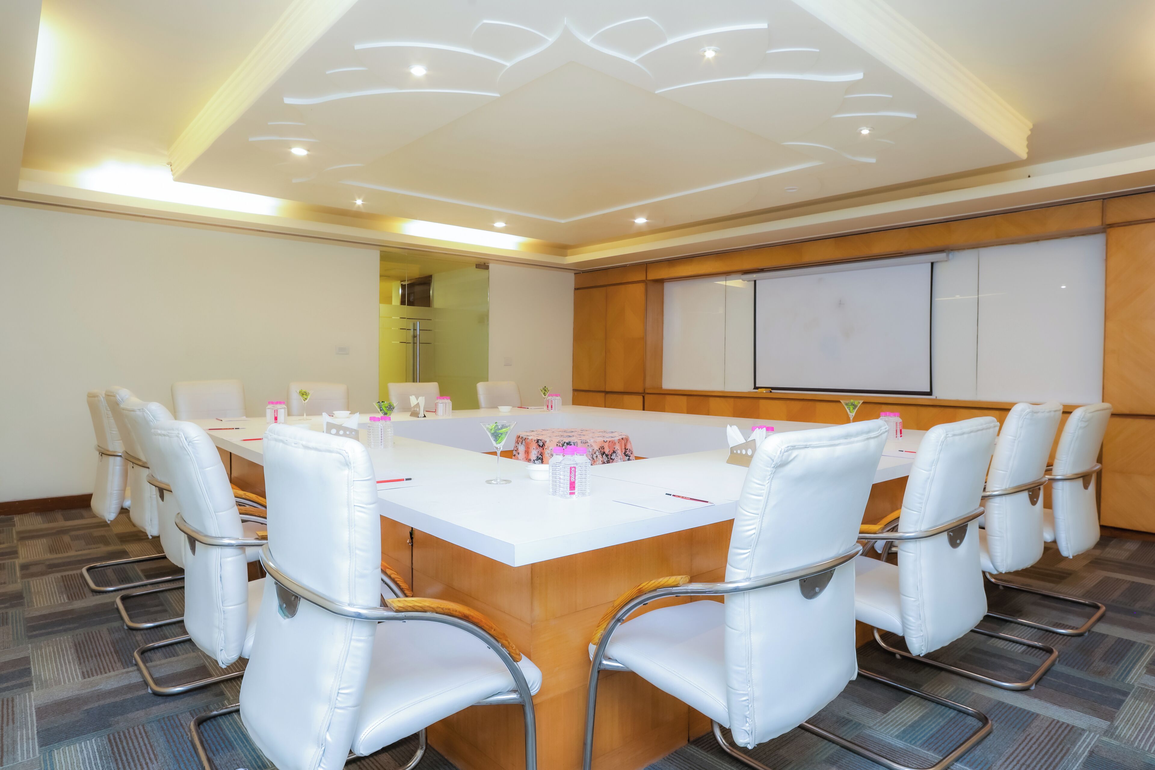 Un salón de conferencias con una mesa grande, sillas blancas y una pantalla de presentación.