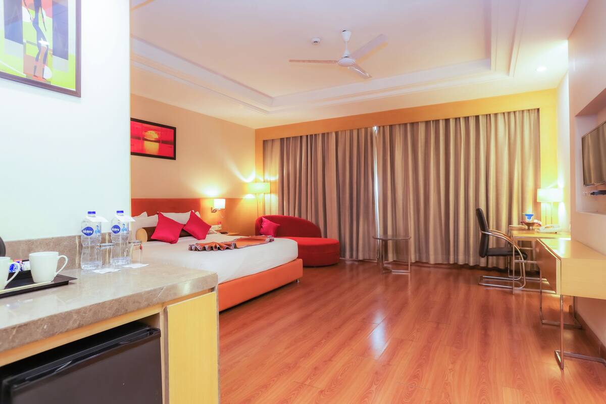 A hotel room with a bed, a desk, a chair, a TV, and a ceiling fan.