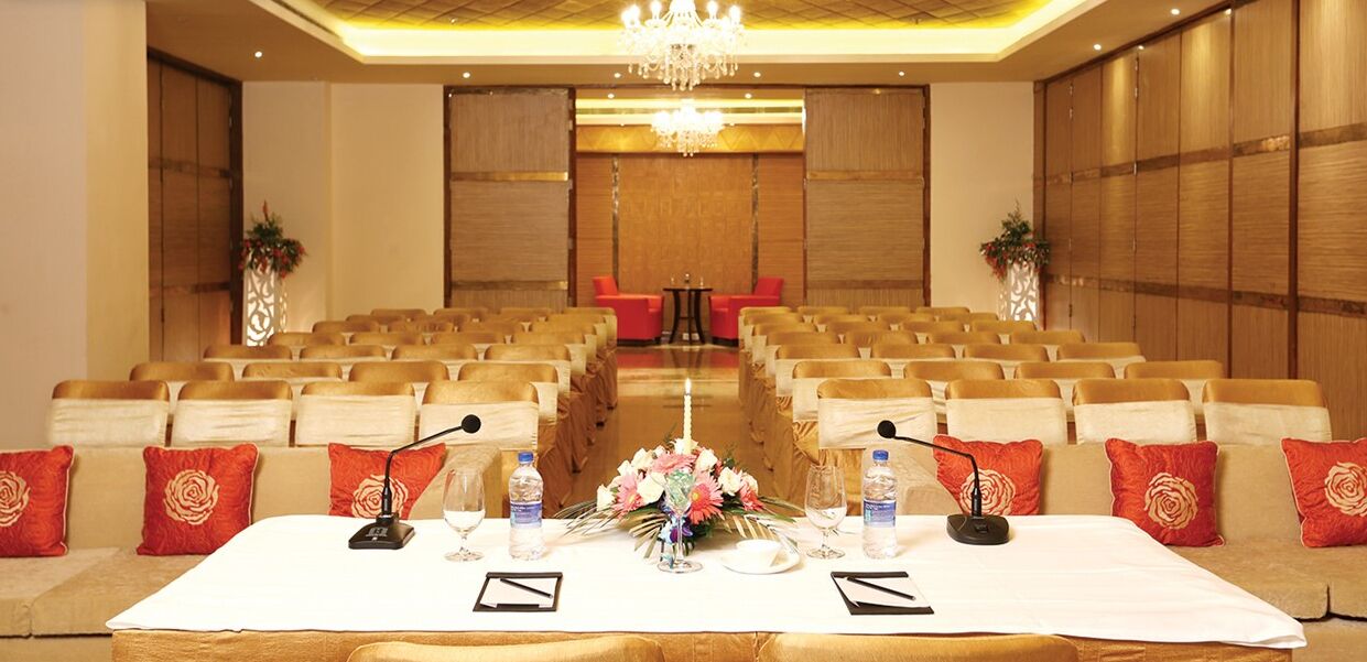 A conference room with rows of chairs, a long table with microphones, and a chandelier.