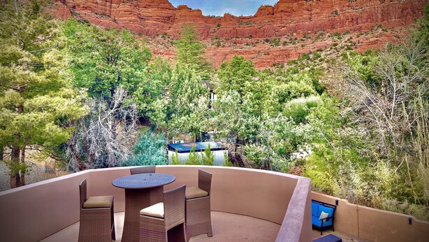 Une terrasse dotée de meubles en osier et d’une table, entourée de verdure et offrant une vue sur des formations rocheuses rouges.
