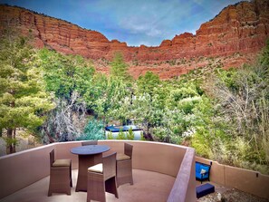 Une terrasse dotée de meubles en osier et d’une table, entourée de verdure et offrant une vue sur des formations rocheuses rouges.