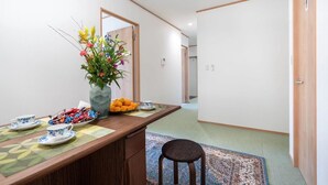 A traditional Japanese-style room with tatami flooring, a low wooden table with a vase of flowers, a plate of oranges, and a tea set. - 1 bedroom apartment in saitama (川口市西川口)