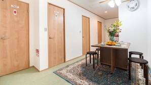 A hotel room with wooden doors, a dining area with a table and chairs, a clock on the wall, and a ceiling fan. - 1 bedroom apartment in saitama (川口市西川口)