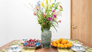 A table with a vase of flowers, a bowl of oranges, and a plate of assorted candies. - 1 bedroom apartment in saitama (川口市西川口)