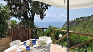 A table set outdoors with a view of the sea, surrounded by greenery and a wooden fence.