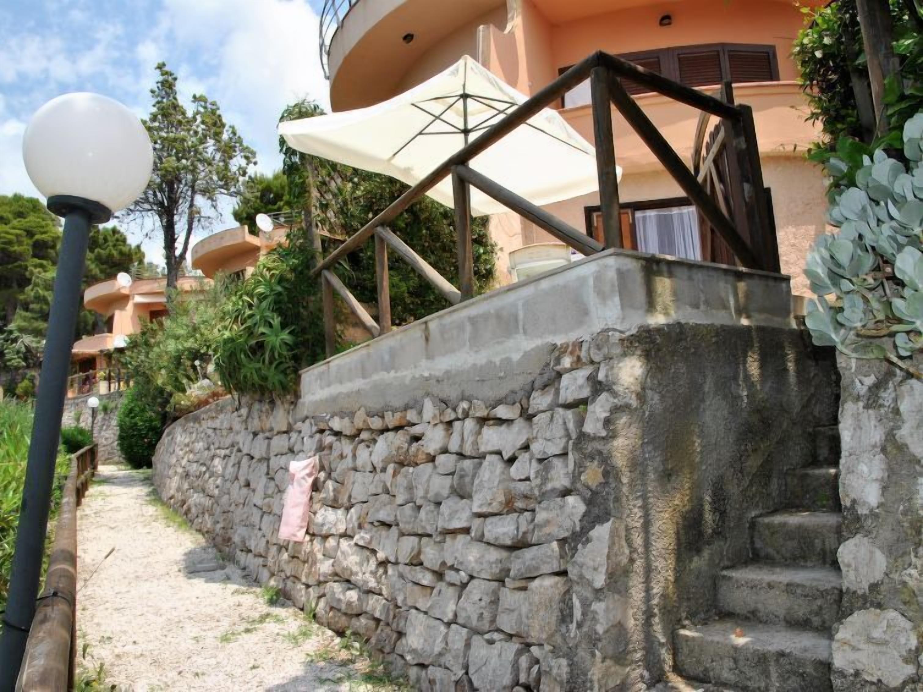 A stone wall with a staircase leading to a building with a balcony.