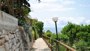 A stone pathway with a wooden railing, leading to a view of the sea.