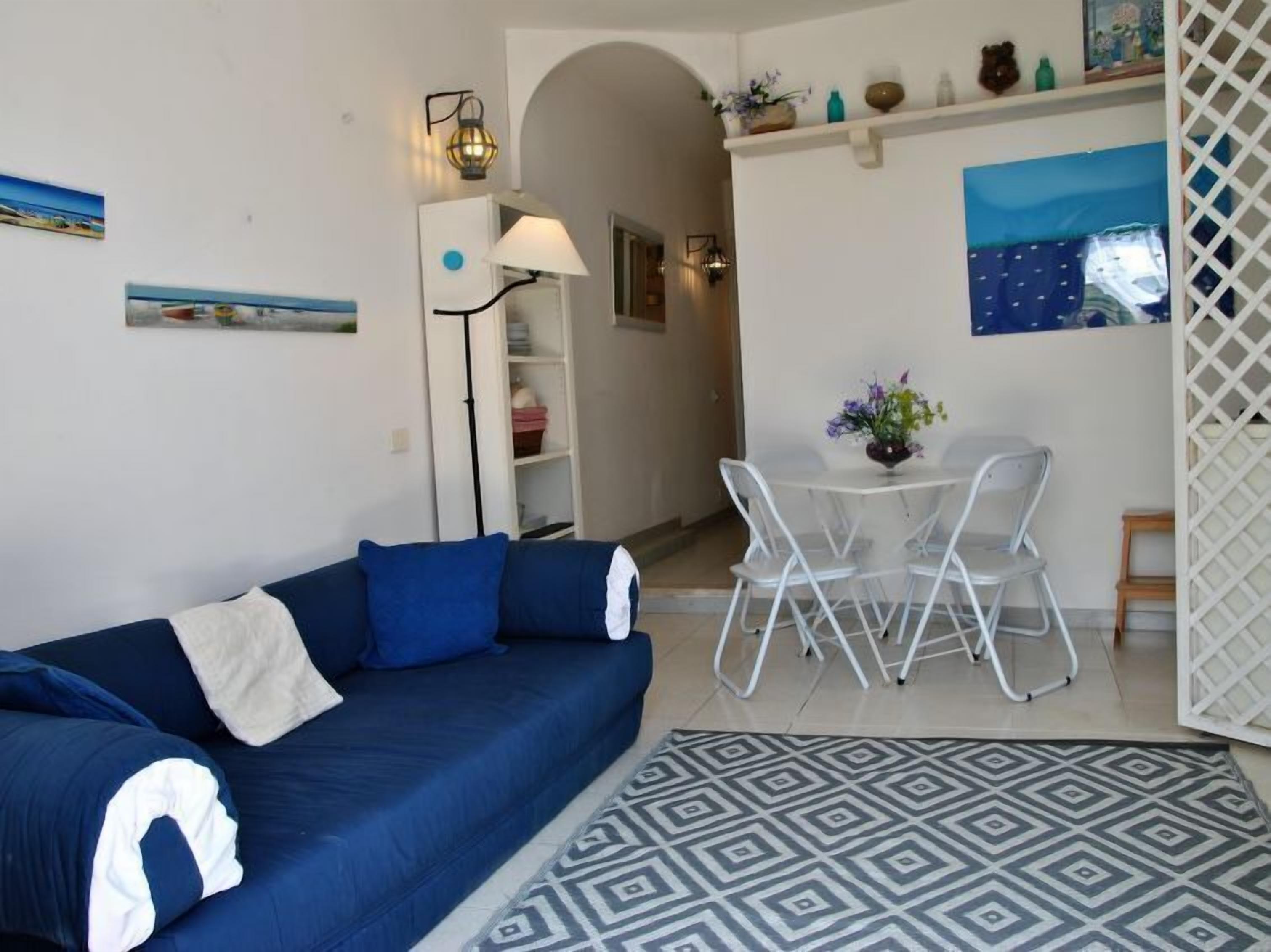 Ein Wohnzimmer mit blauem Sofa, einem Esstisch mit Stühlen, einem gemusterten Teppich und einer weißen Trennwand.
