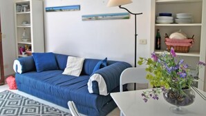 A modern living room with a blue sofa, a white table with a vase of flowers, and a floor lamp.