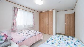A bedroom with two beds, a wooden wardrobe, a window with curtains, and a ceiling light.