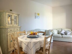 Un área de comedor con una mesa lista para dos personas, un mueble con cajones y un sofá a rayas al fondo.
