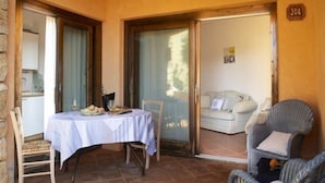 Un coin repas accueillant, avec une table dressée pour deux personnes, une chaise en osier et une vue sur un balcon agrémenté d’un canapé.