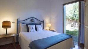 Une chambre à coucher comprenant un lit, deux lampes de chevet, une table de chevet et une fenêtre donnant sur un paysage verdoyant.