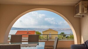 A balcony with wicker furniture, a glass table, and a view of houses and mountains. - Steffano by Interhome (Karlobag)