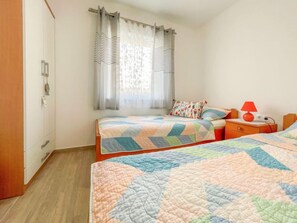 Un dormitorio con dos camas, una mesita de noche, una lámpara y una ventana con cortinas.