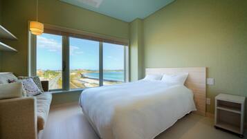 A bedroom with a large bed, a sofa, a view of the sea, and a ceiling fan.