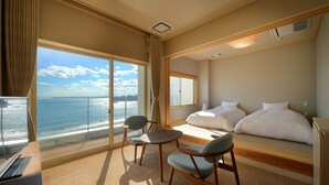 Een hotelkamer met een groot raam met uitzicht op zee, een bed, een bureau en twee stoelen.