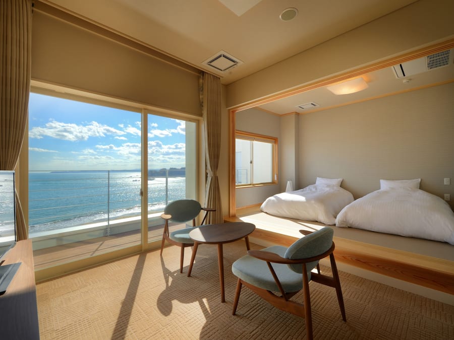 Habitación de hotel con un ventanal grande que da al mar, una cama, un escritorio y dos sillas.