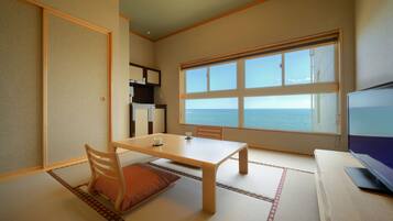 Una habitación con suelo de tatami, una mesa baja con sillas, un televisor y un ventanal con vista al mar.