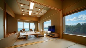 Een traditionele Japanse kamer met tatami vloeren, een lage tafel, stoelen, een televisie en grote ramen met uitzicht op zee.