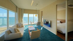 Hotelkamer met groot raam en uitzicht op zee, een bank, een eettafel en een bed.