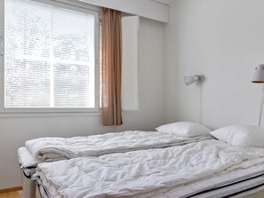 Une pièce simple et dépouillée, avec un lit simple, une fenêtre avec des stores et une lampe fixée au mur.