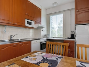 A compact kitchen with wooden cabinets, a microwave, a stove, a sink, and a window with blinds. - Outapailakka j 12 by Interhome (Inari)