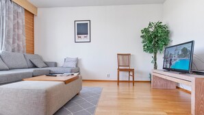A modern living room with a grey sofa, a wooden coffee table, a wooden chair, a TV on a wooden stand, and a potted plant. - Outapailakka j 12 by Interhome (Inari)