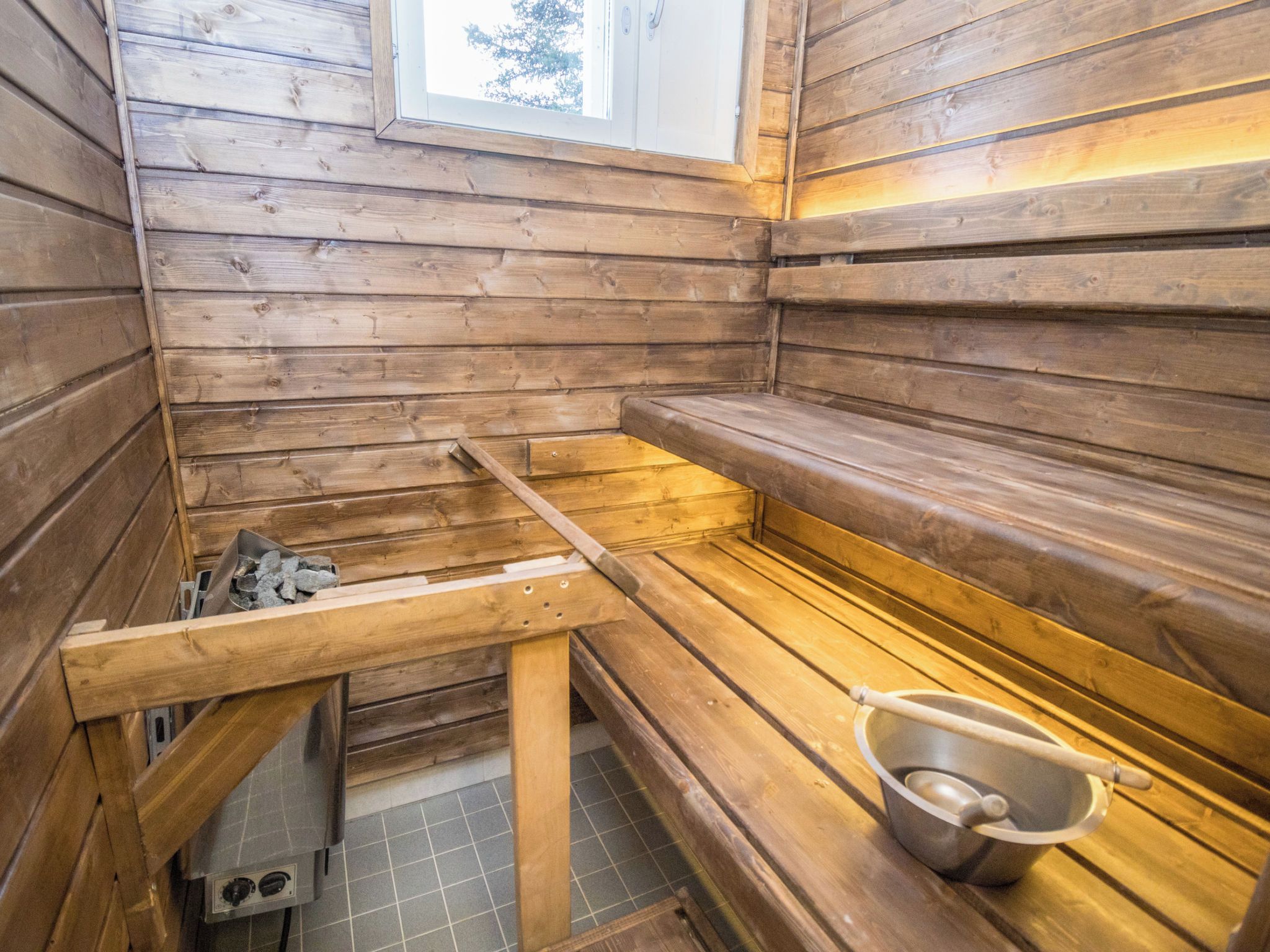 A sauna room with wooden benches, a metal bucket, and a window.