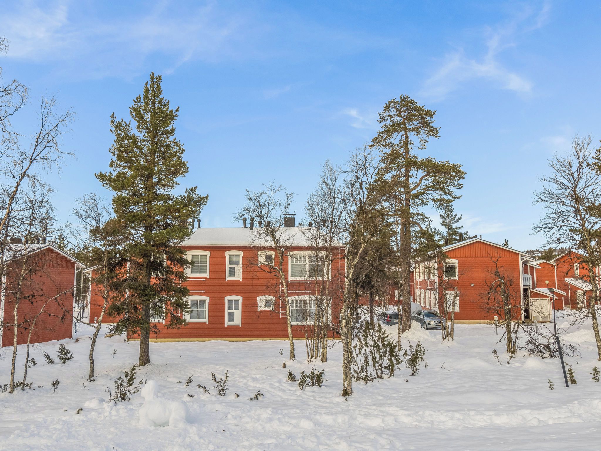 A red brick building with multiple windows, surrounded by snow-covered ground and bare trees.