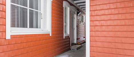 A red wooden house with white trim, a covered porch, and a visible door leading to a garage.