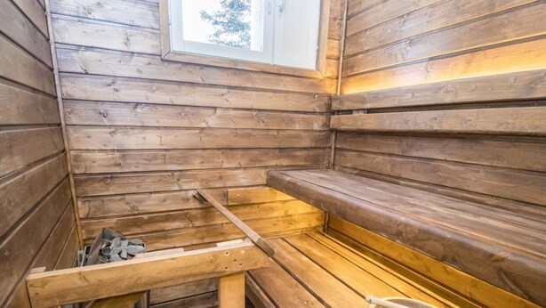 Un sauna con bancos de madera, un balde de metal y una ventana.