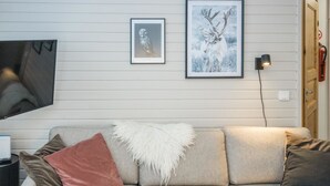 Una sala de estar con un sofá gris, un plaid blanco mullido y dos cuadros en la pared.