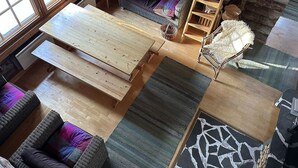 Een gezellig blokhutinterieur met een grote houten eettafel, rieten meubels en een wand van boomstammen.