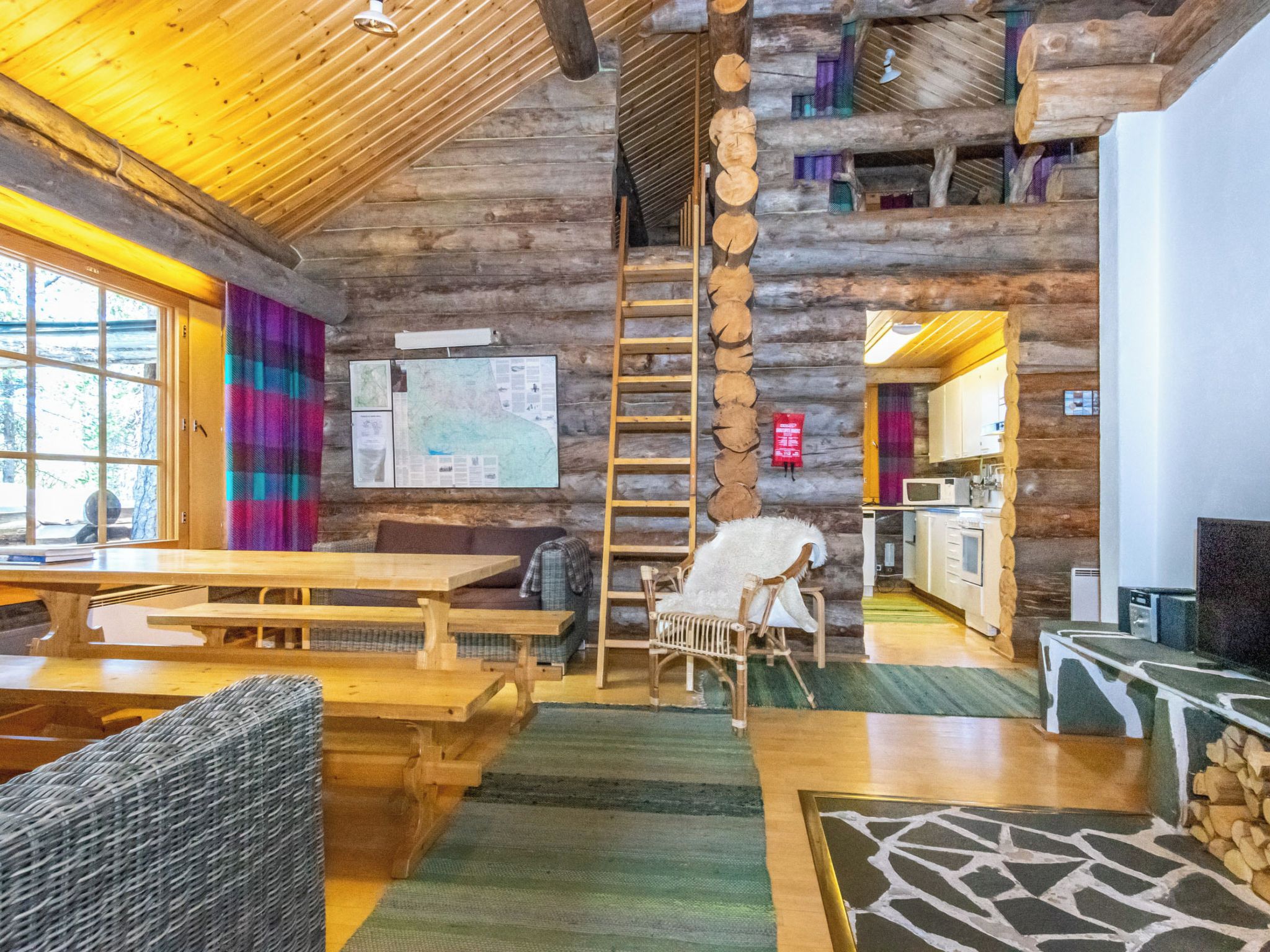 Ein rustikales Holzhaus-Interieur mit Holztisch, Stühlen, einer Leiter und einer Küchenzeile.