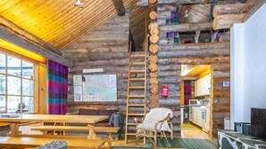 Een rustiek houten interieur met een eettafel, een bank, een ladder en een keukenhoek.