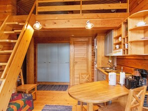 Un intérieur de chalet en bois compact, comprenant un coin repas, une cuisine et une chambre à coucher située en mezzanine.