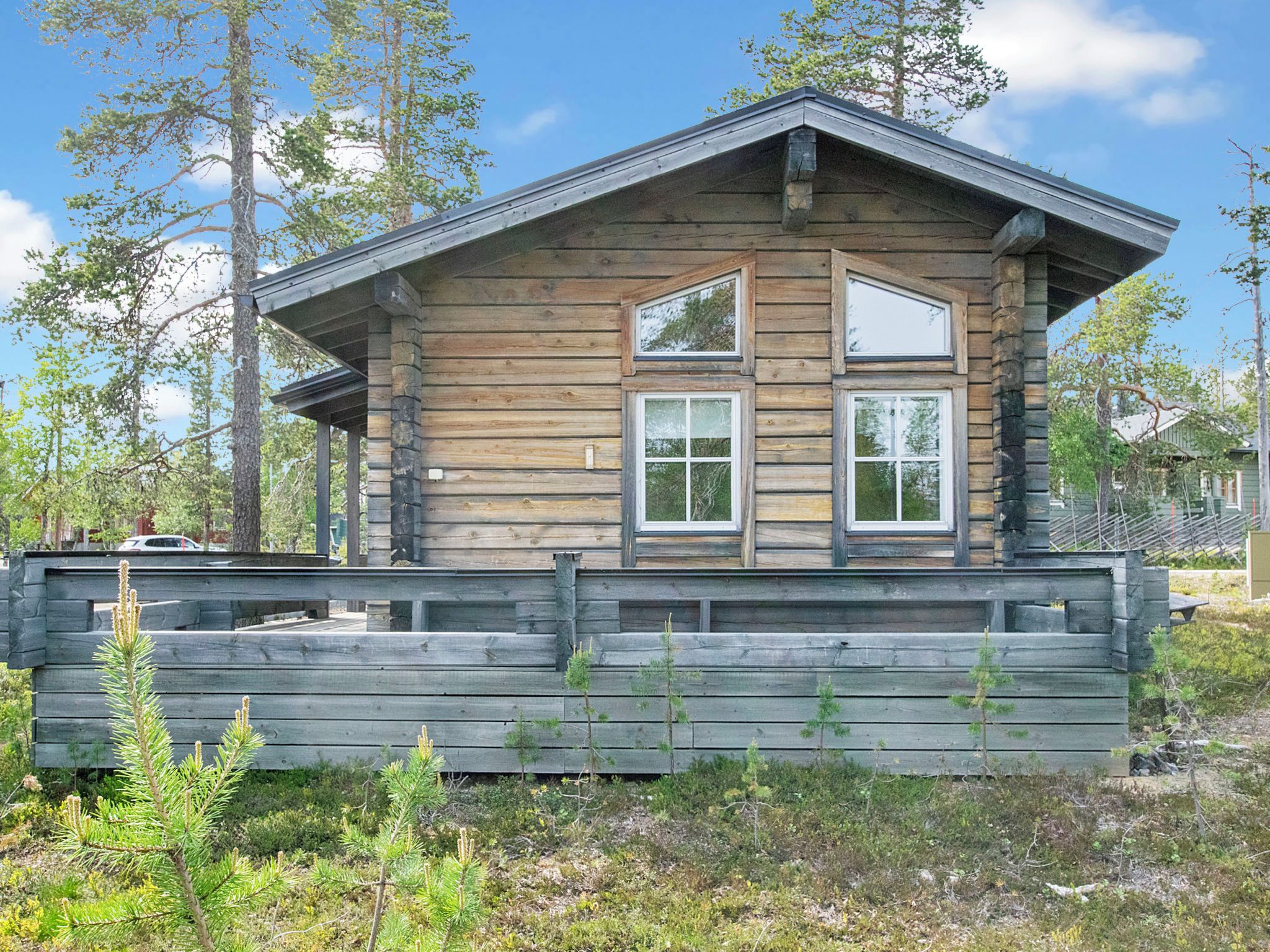 A wooden cabin with a gabled roof, two windows, and a wooden deck in front.