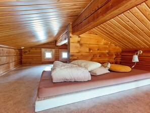 A cozy attic bedroom with a wooden sloped ceiling, a bed with pillows, and a small window.