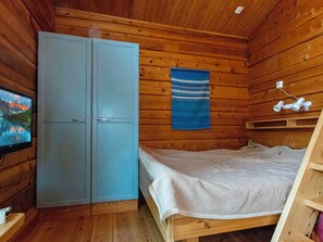 Ein Zimmer mit einem Bett, einem Kleiderschrank, einem an der Wand befestigten Fernseher und einem blauen Wandbild.