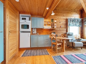 Une cuisine compacte équipée d’un four à micro-ondes, d’un four traditionnel et de placards, un coin repas avec une table et des chaises, et une fenêtre avec des rideaux.