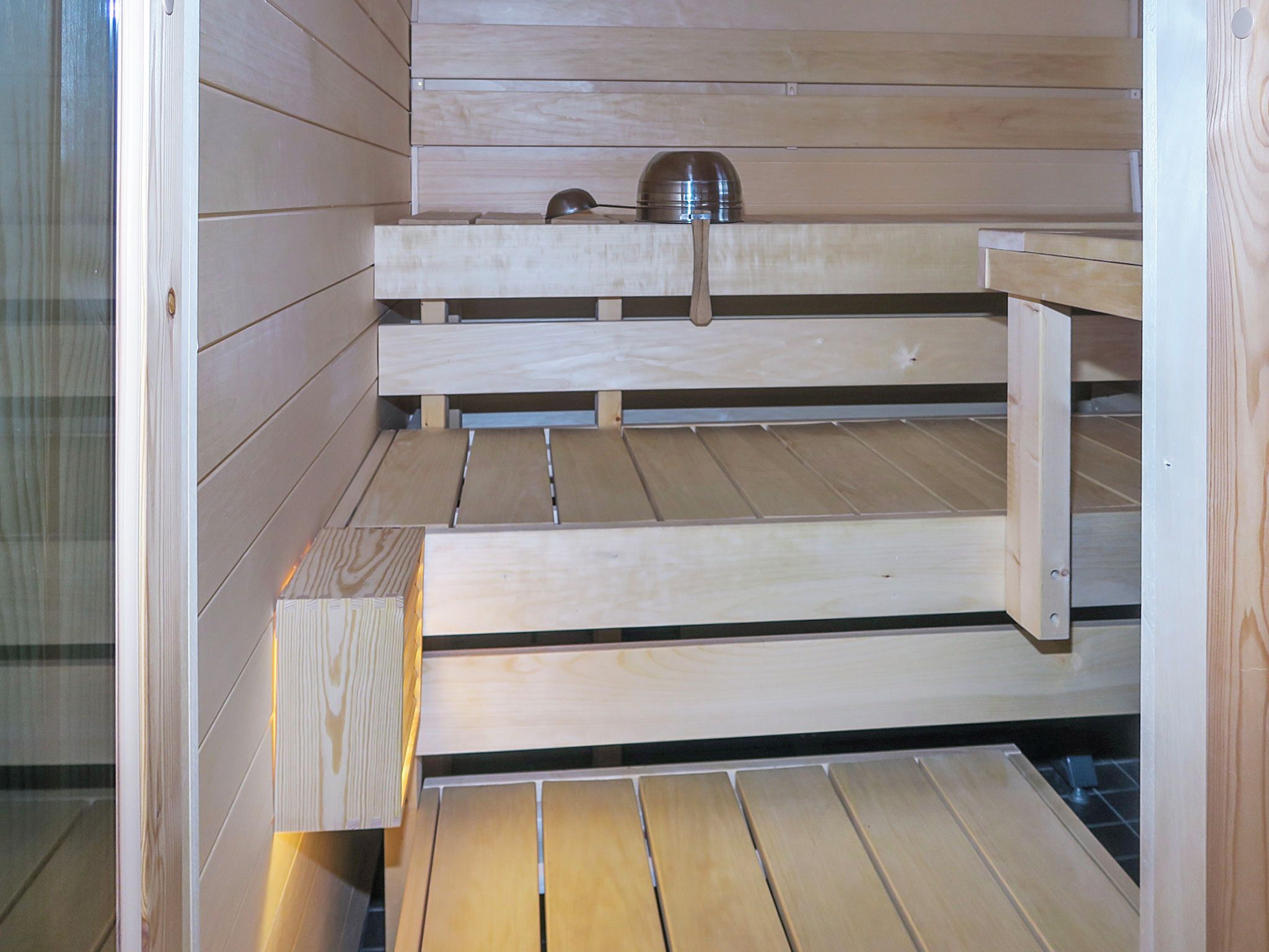 Una sauna con panche in legno e un contenitore metallico sullo scaffale superiore.